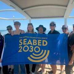 staff and students about the RV Falkor hold up a banner