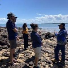 A photo of people standing on the shore listening to an Elder