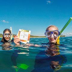 Two girls in the water 0wearing dive masks hold up a copy of their CoralWatch coral health chart.